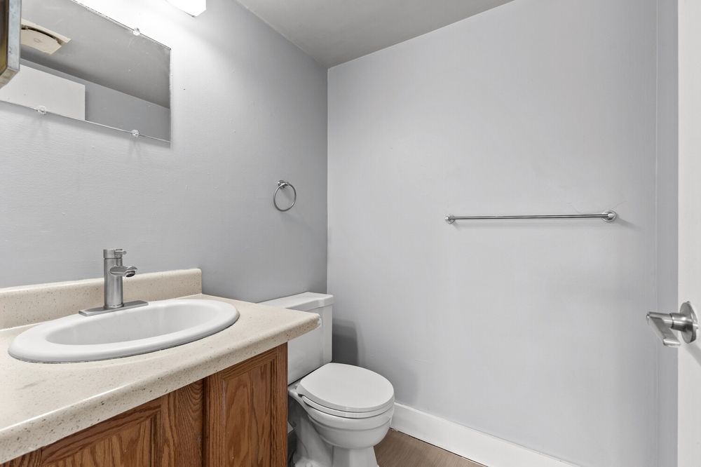 Half bathroom with wood vanity, white sink, chrome faucet, toilet, and large mirror above the counter.