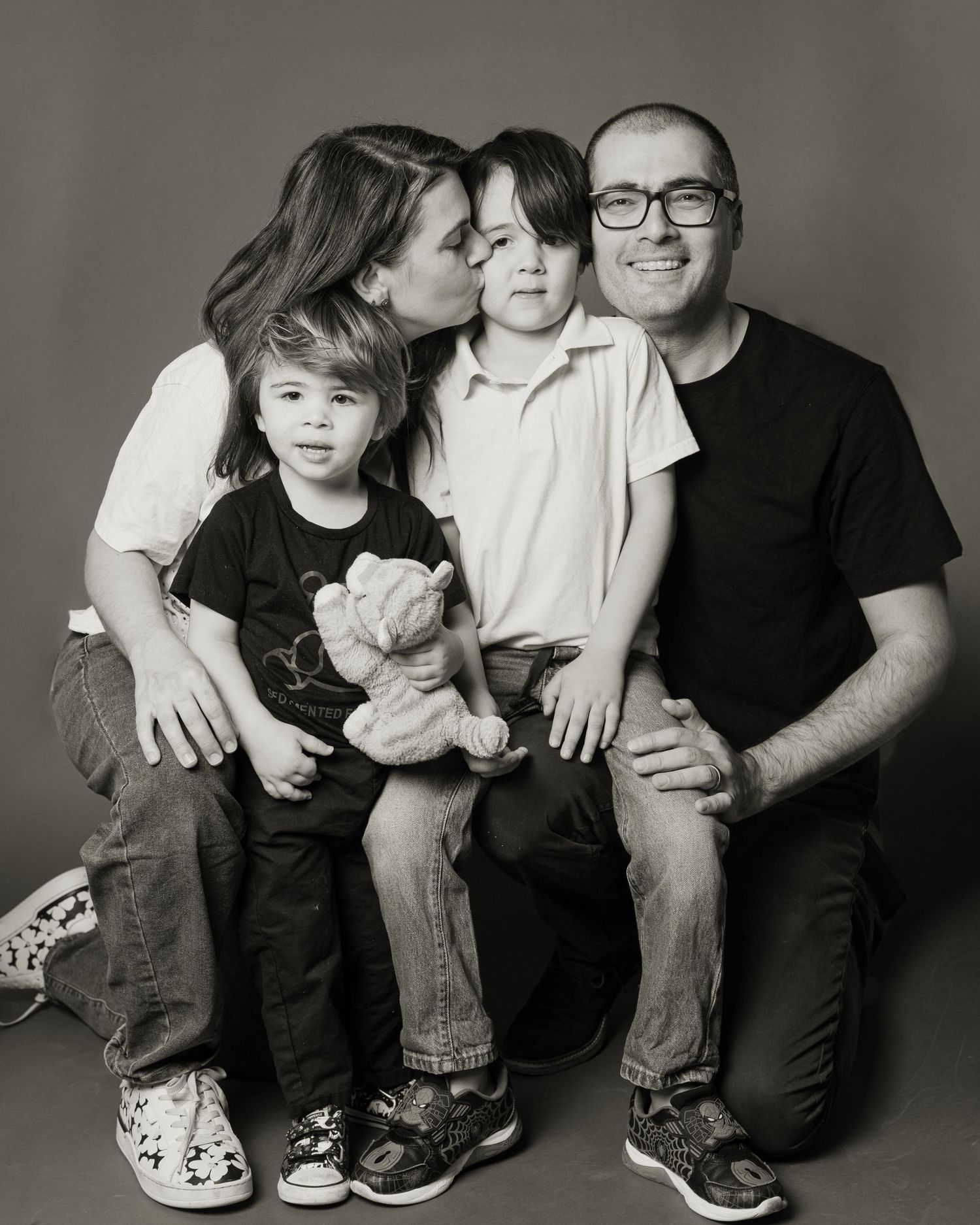 Family of four posing joyfully in front of a decorative Easter backdrop with flowers, eggs, and greenery.