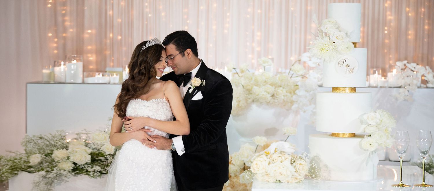 Bride and groom sharing romantic kiss beside tiered white wedding cake with floral decorations.