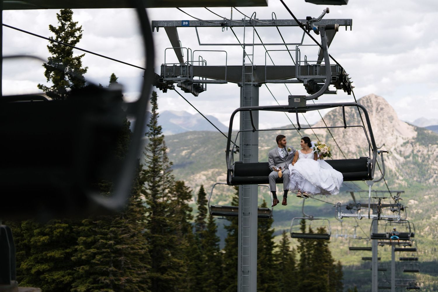 Bride and groom ride a ski lift together at a mountain resort on their wedding day.