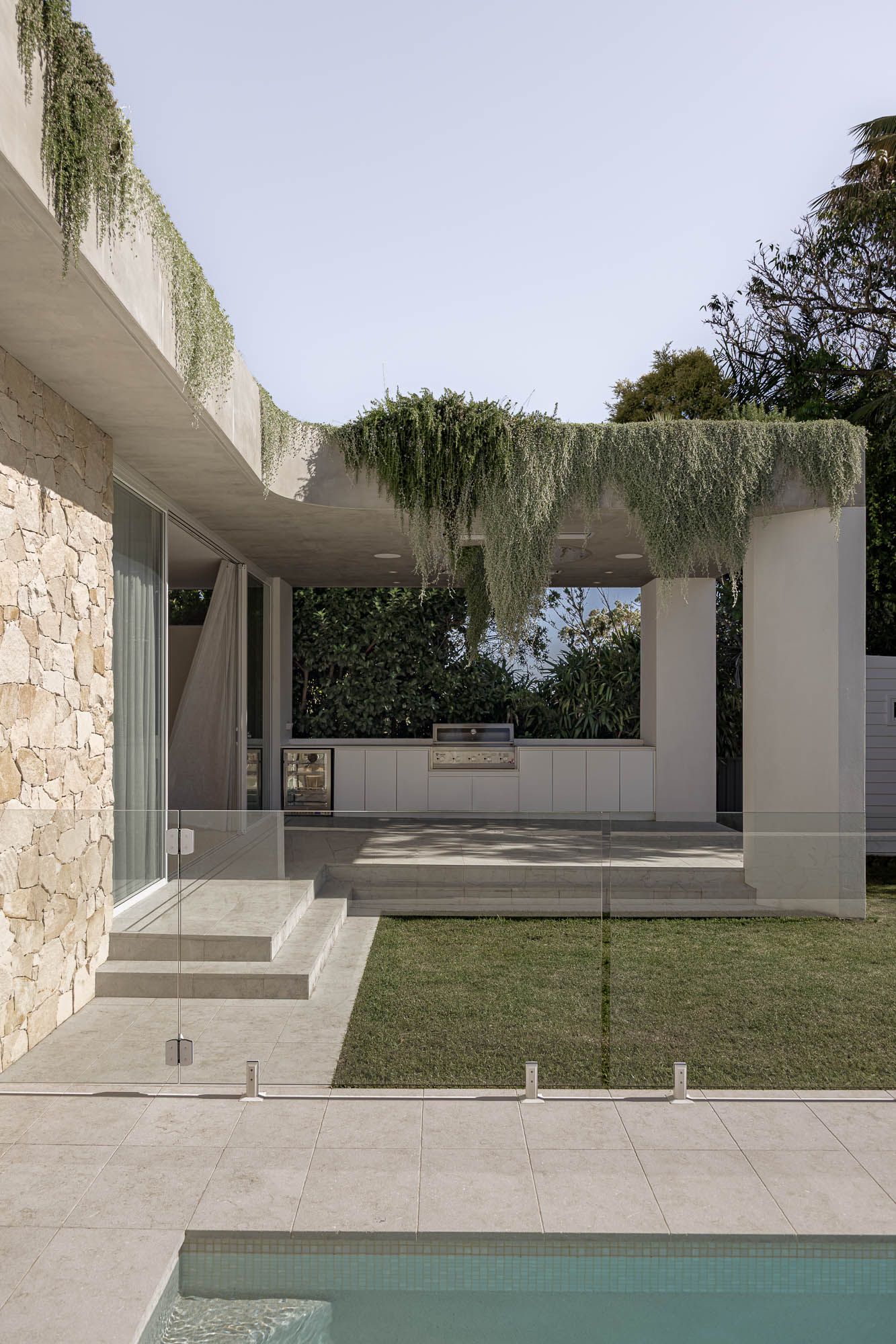 Exterior architectural photography of an outdoor kitchen and pool area beneath a planted concrete pergola, captured in Port Hacking, Sutherl
