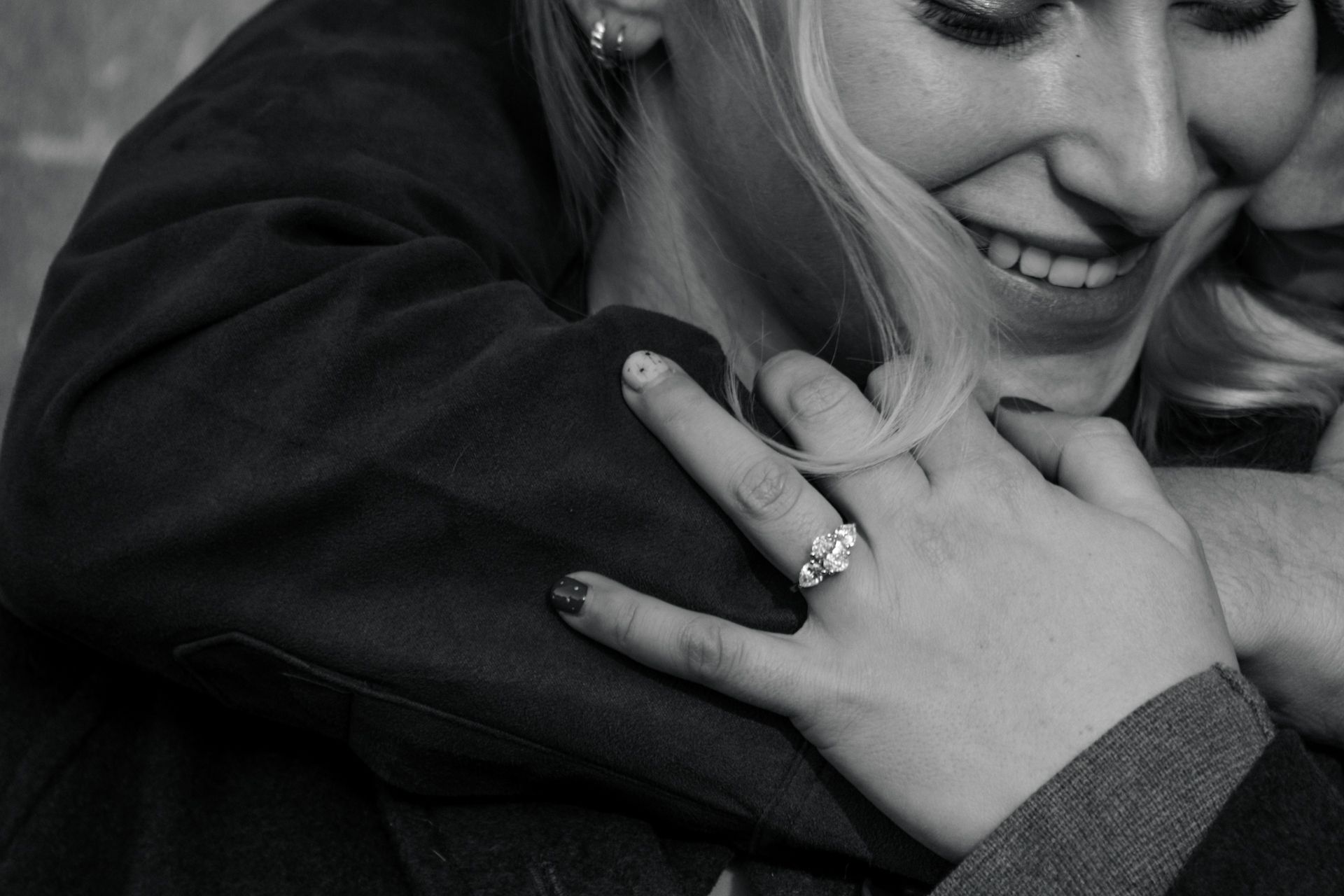 Black and white photo of a couple embracing, showcasing a sparkling engagement ring on the woman's hand.