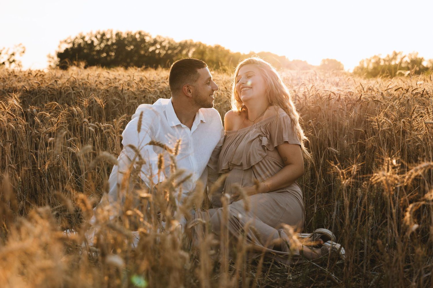 Romantic couple sitting together in a golden wheat field bathed in warm sunset light.