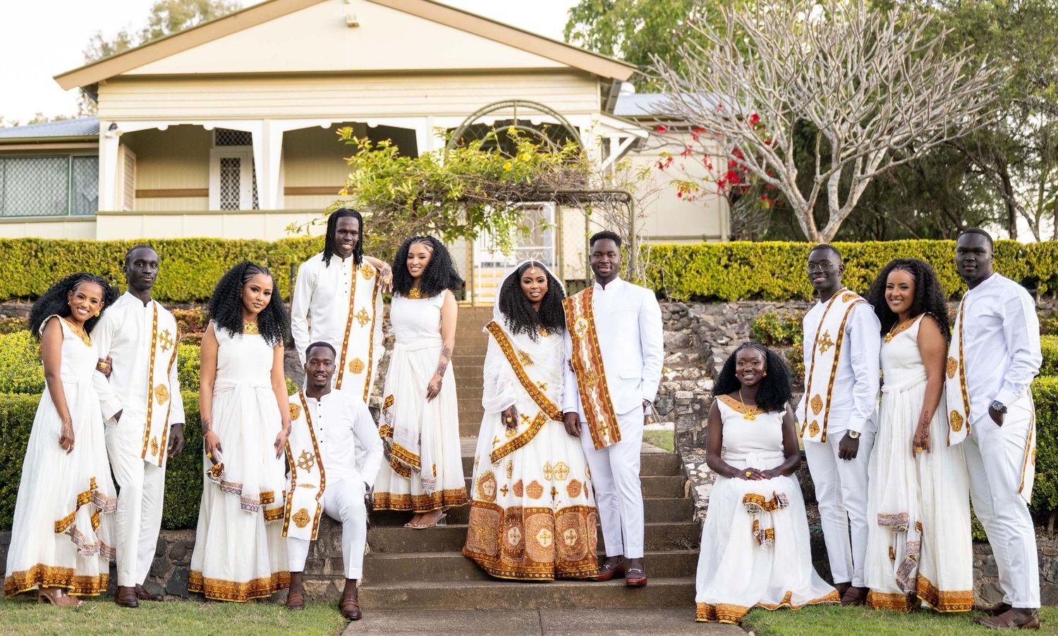 Group of people in matching white and gold traditional African attire posing outdoors at a celebratory event.
