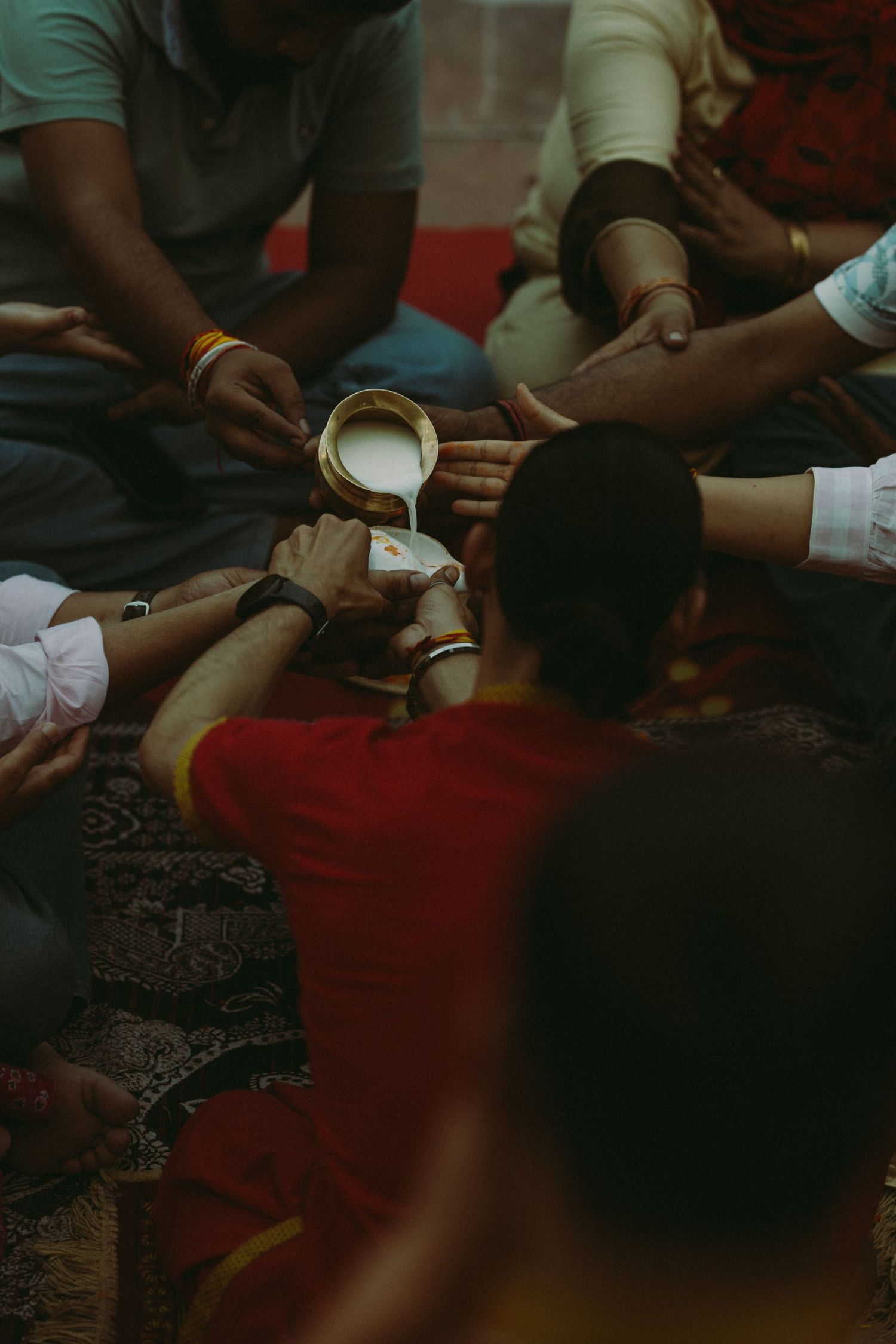Group of people gathered around small cup during traditional Indian ceremony or ritual.