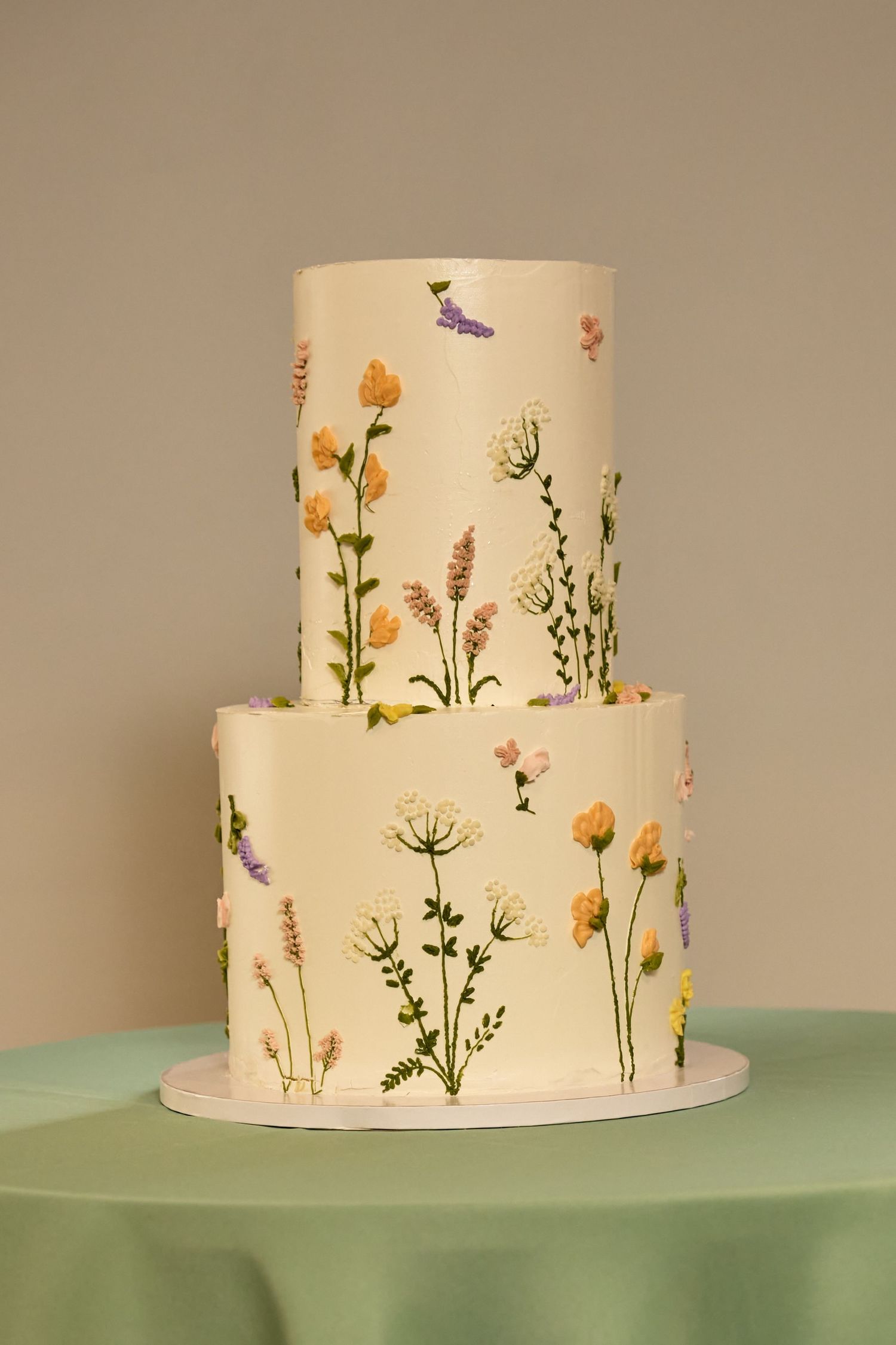 Two-tier white wedding cake decorated with colorful hand-painted wildflowers and butterflies on a mint green tablecloth.