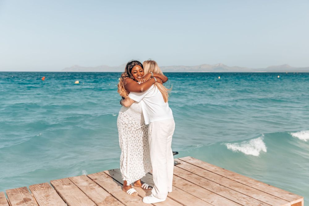 A joyful couple tightly embracing on a wooden pier by the sea during a surprise same-sex proposal session in Mallorca.