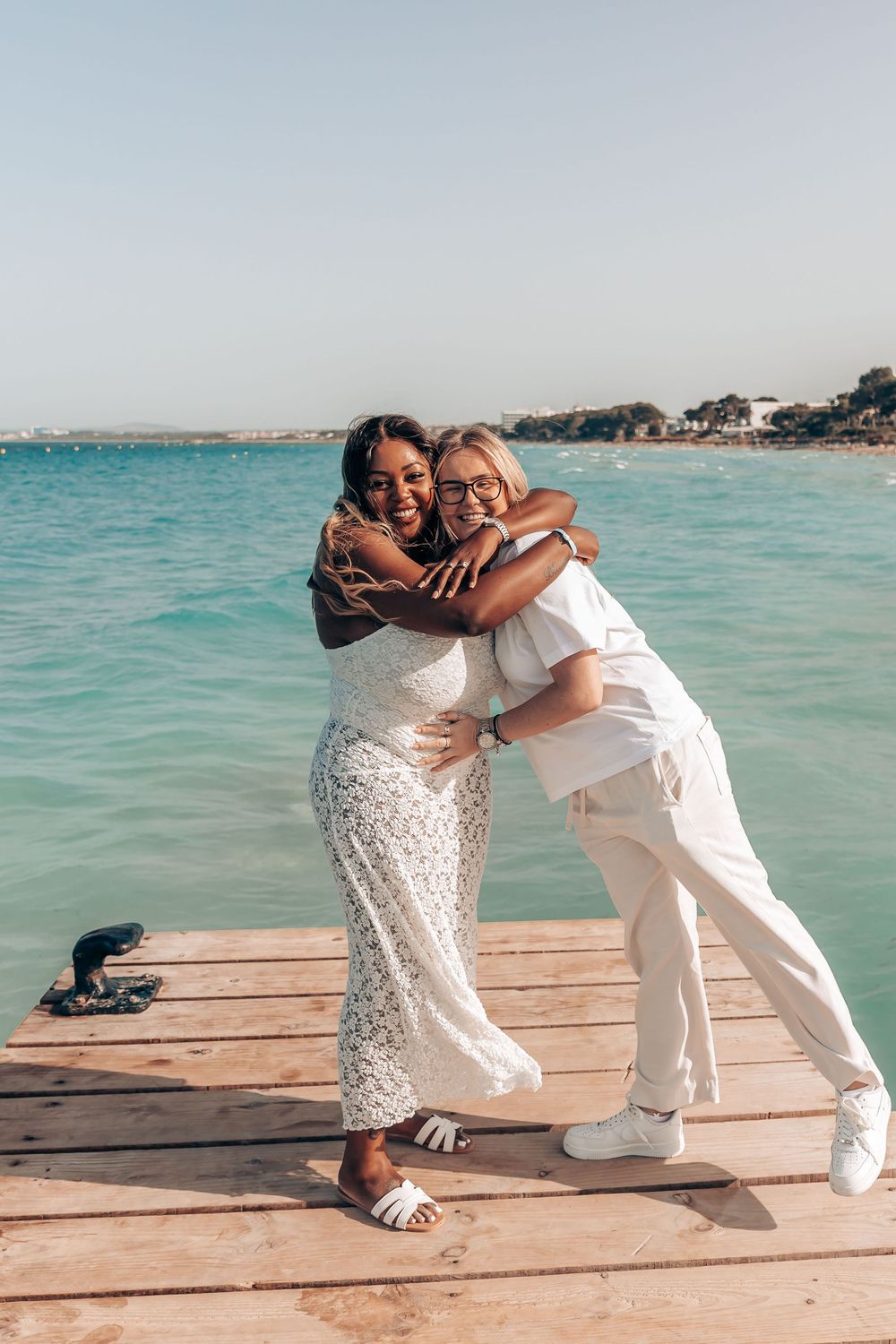 A woman hugging her fiancée in a joyful embrace on a wooden pier after a successful Mallorca surprise proposal.
