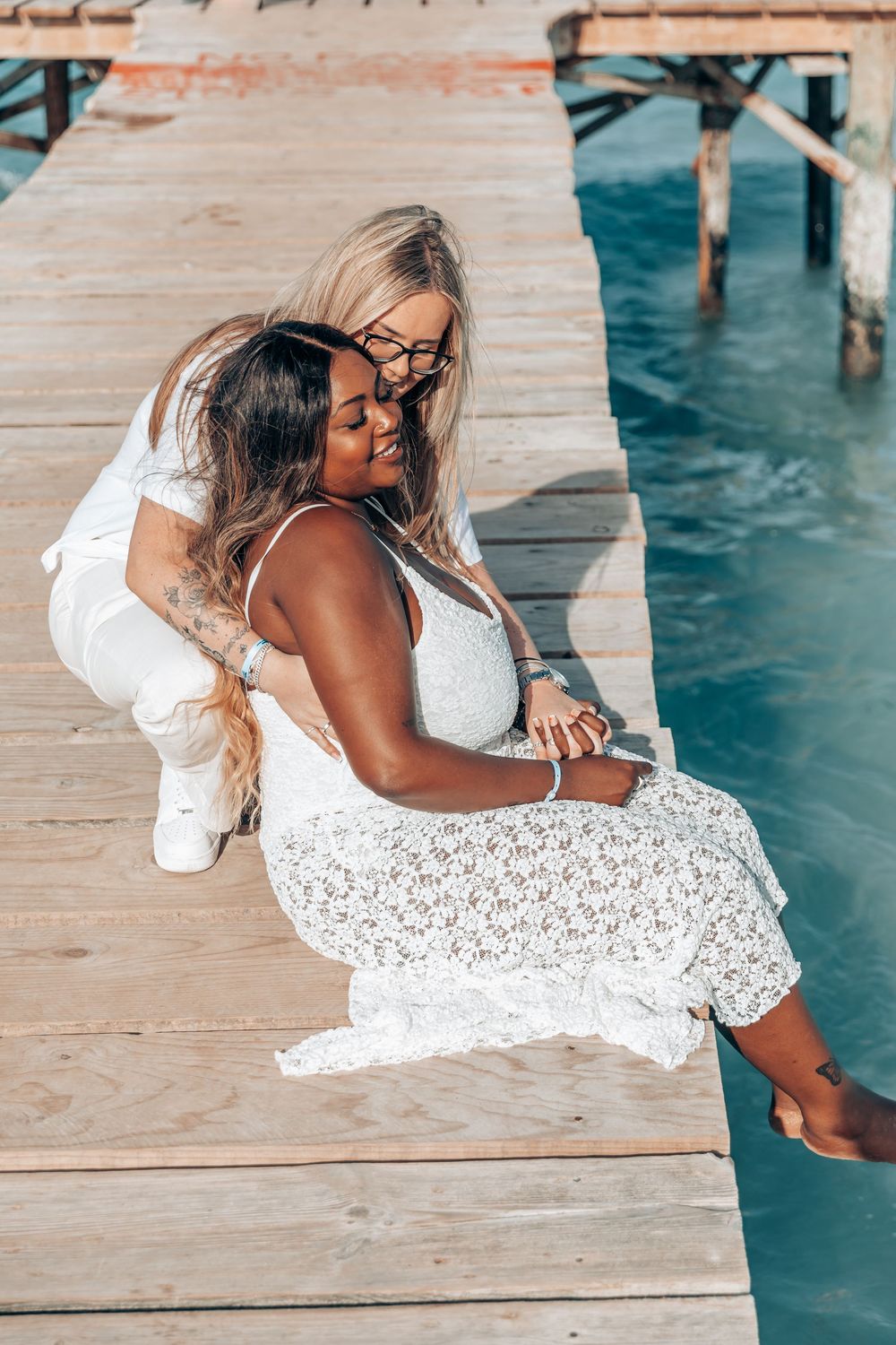 High-angle shot of a couple holding each other closely while relaxing on a wooden dock during their surprise same-sex proposal session in Ma