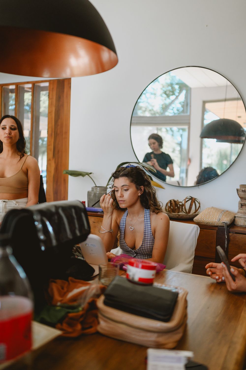 Bridesmaid applying makeup at a wooden table with a round mirror in background.