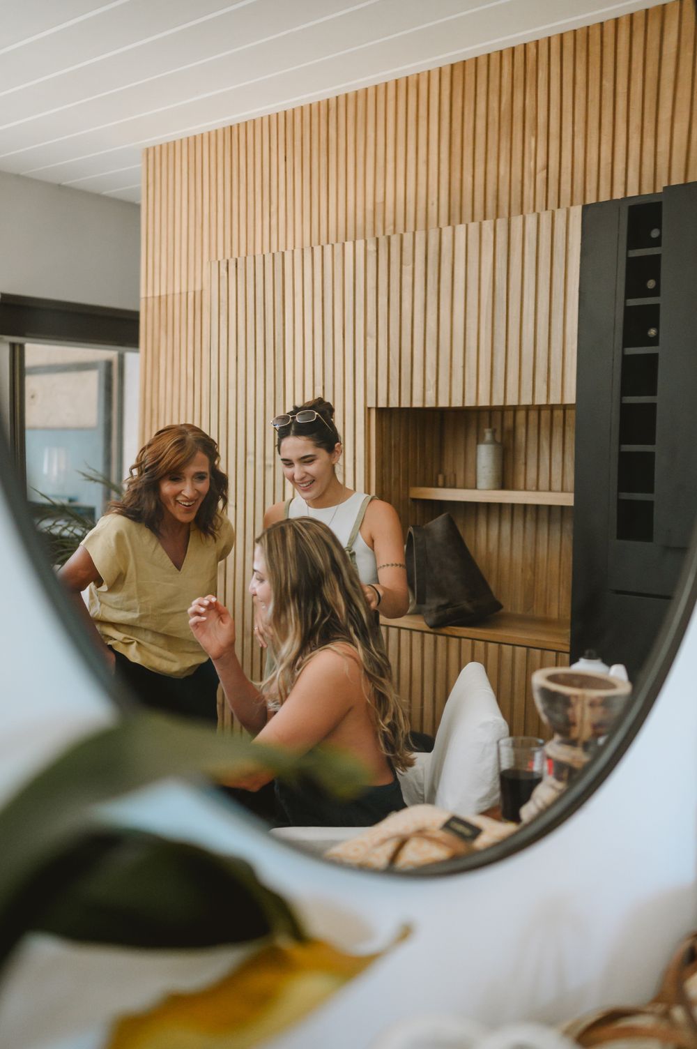 Three women laughing and chatting in a modern salon with wooden slat wall decor.
