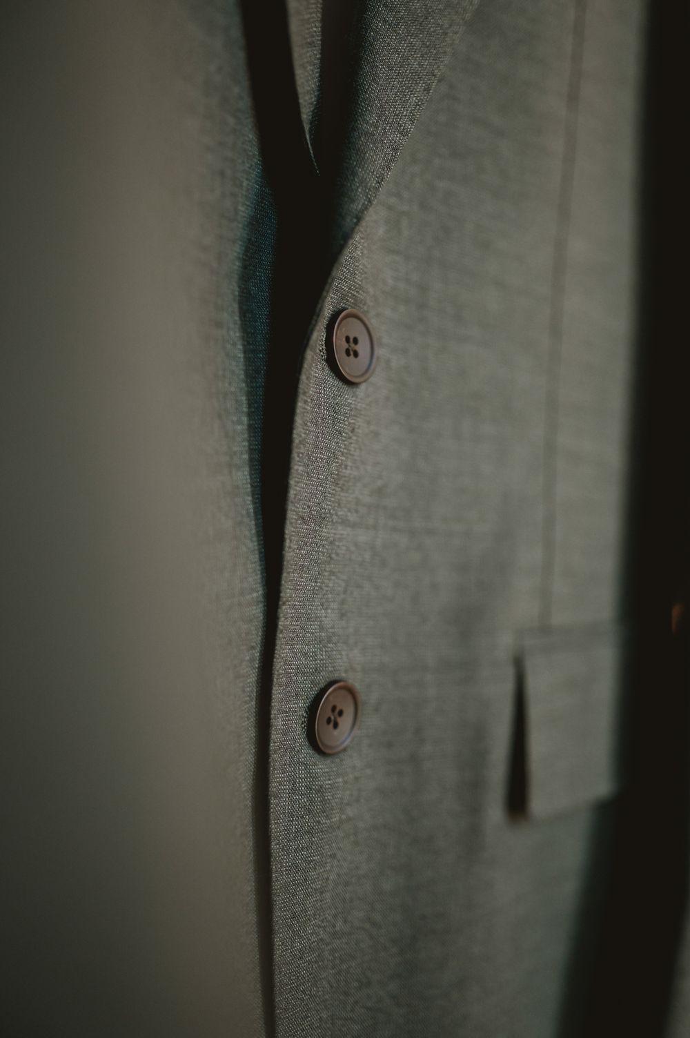 Close-up of a gray suit jacket with brown buttons hanging in soft shadow lighting.