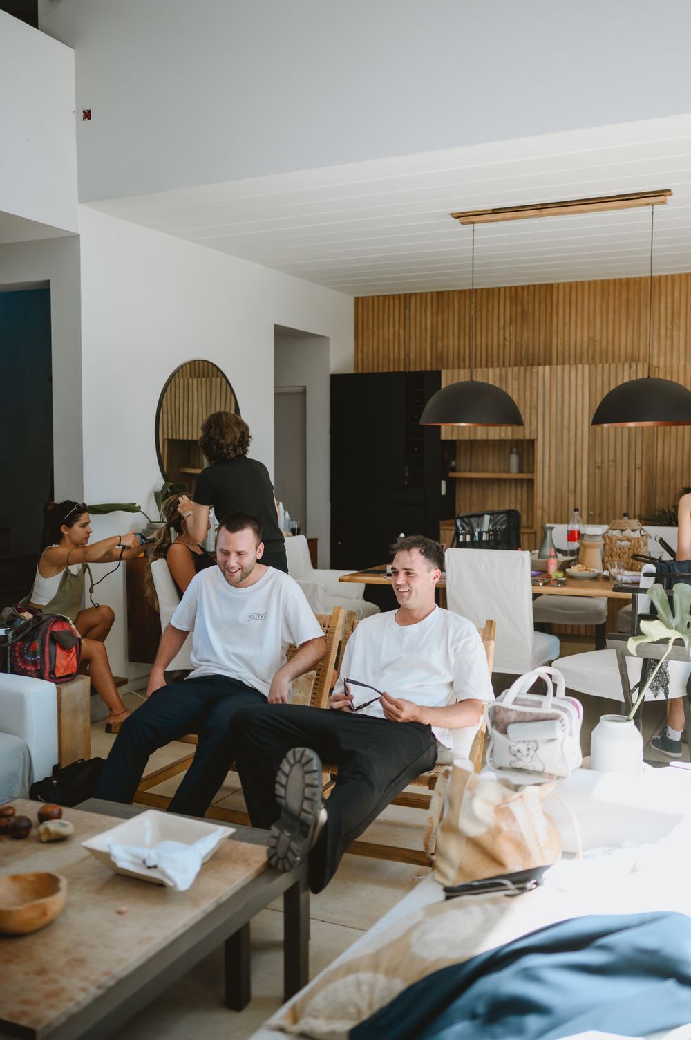 Two men in white t-shirts relaxing in modern living room during wedding preparations.