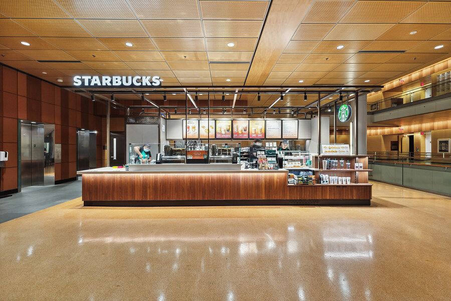 Modern Starbucks coffee counter with wood paneling in a spacious open lobby with warm lighting.