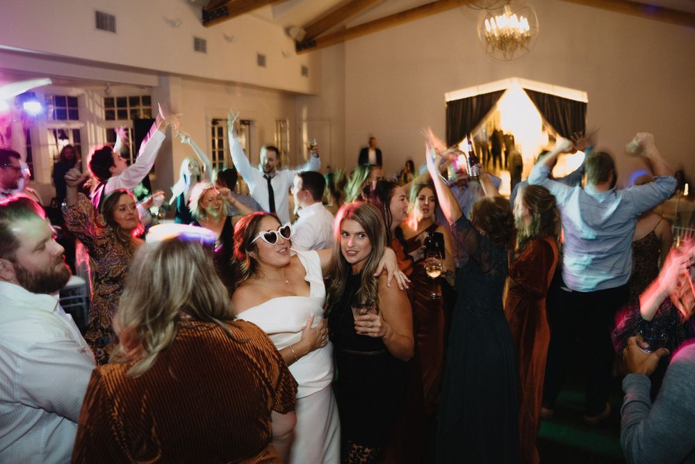 Guests dancing and celebrating at a lively wedding reception with colorful lights.
