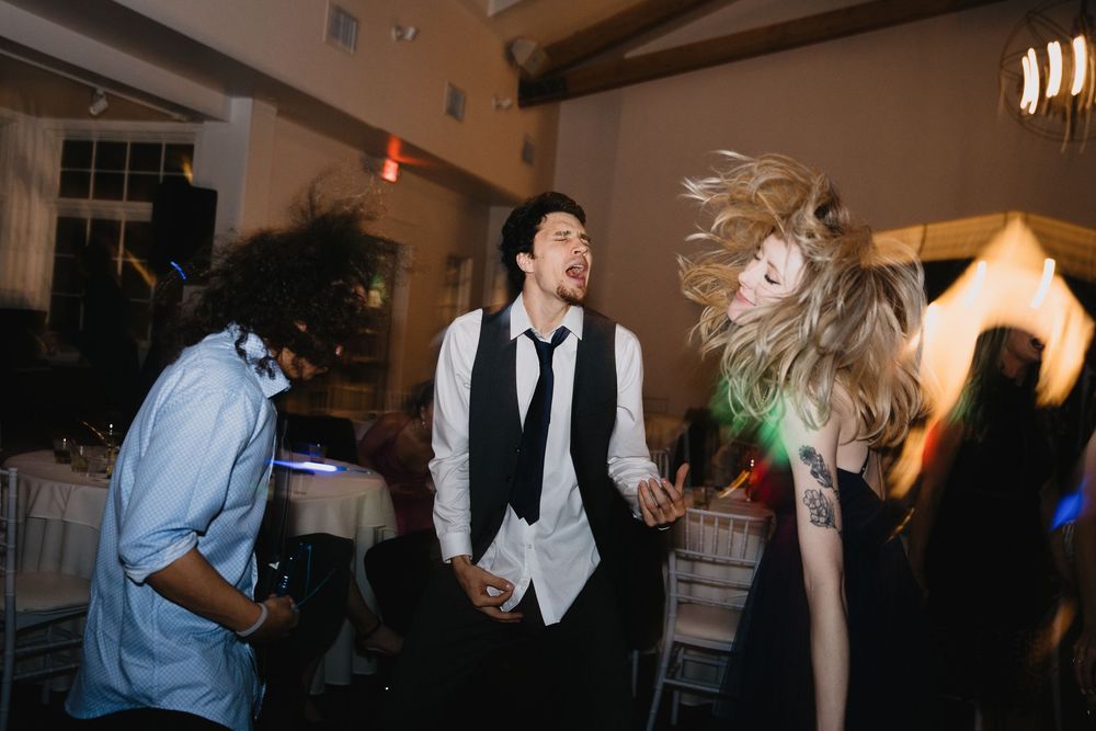 Man in vest and tie dancing energetically with guests at a wedding reception.