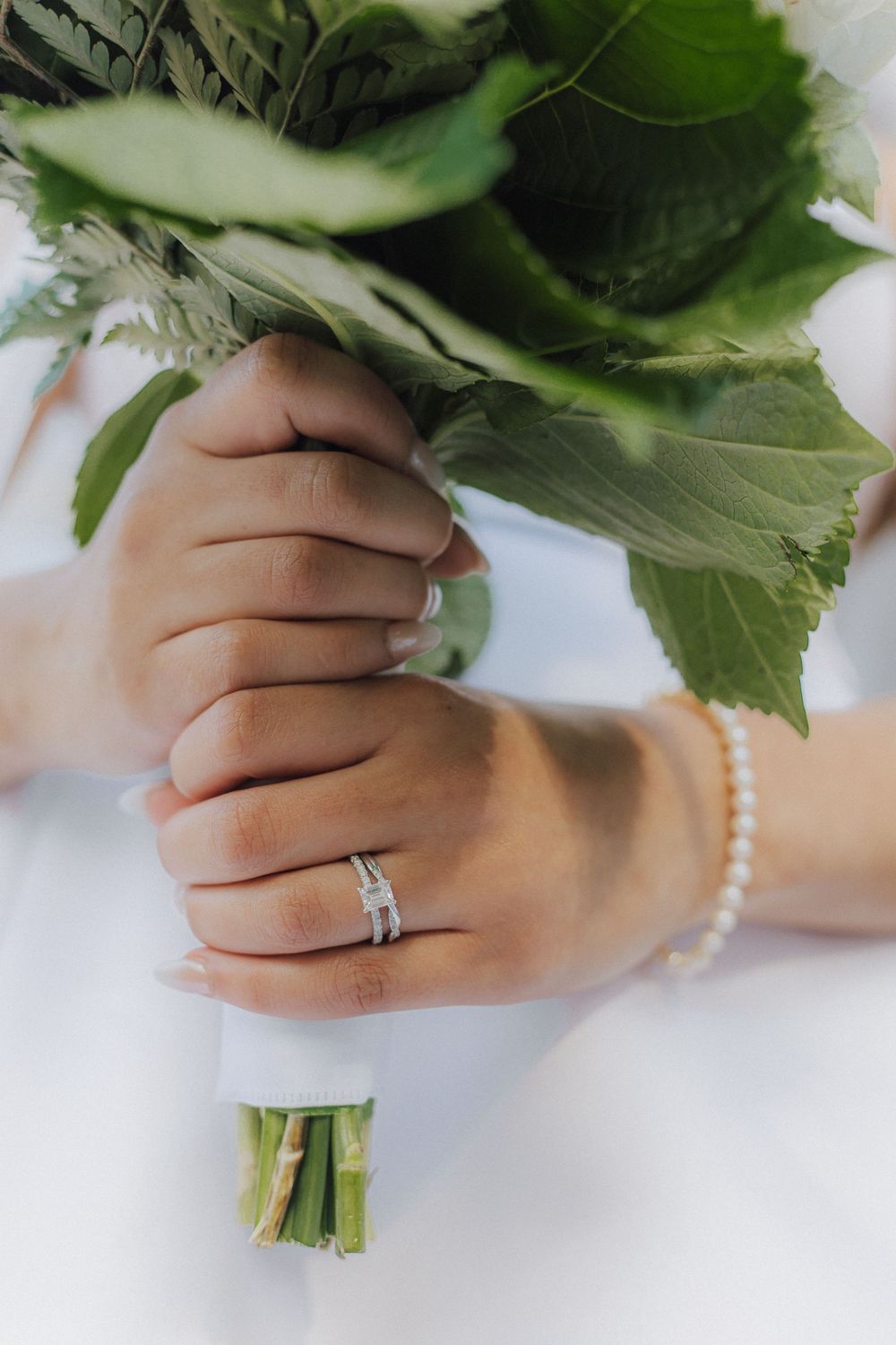 Close-up of hands holding a wedding bouquet, showing pearl bracelet and engagement ring details.