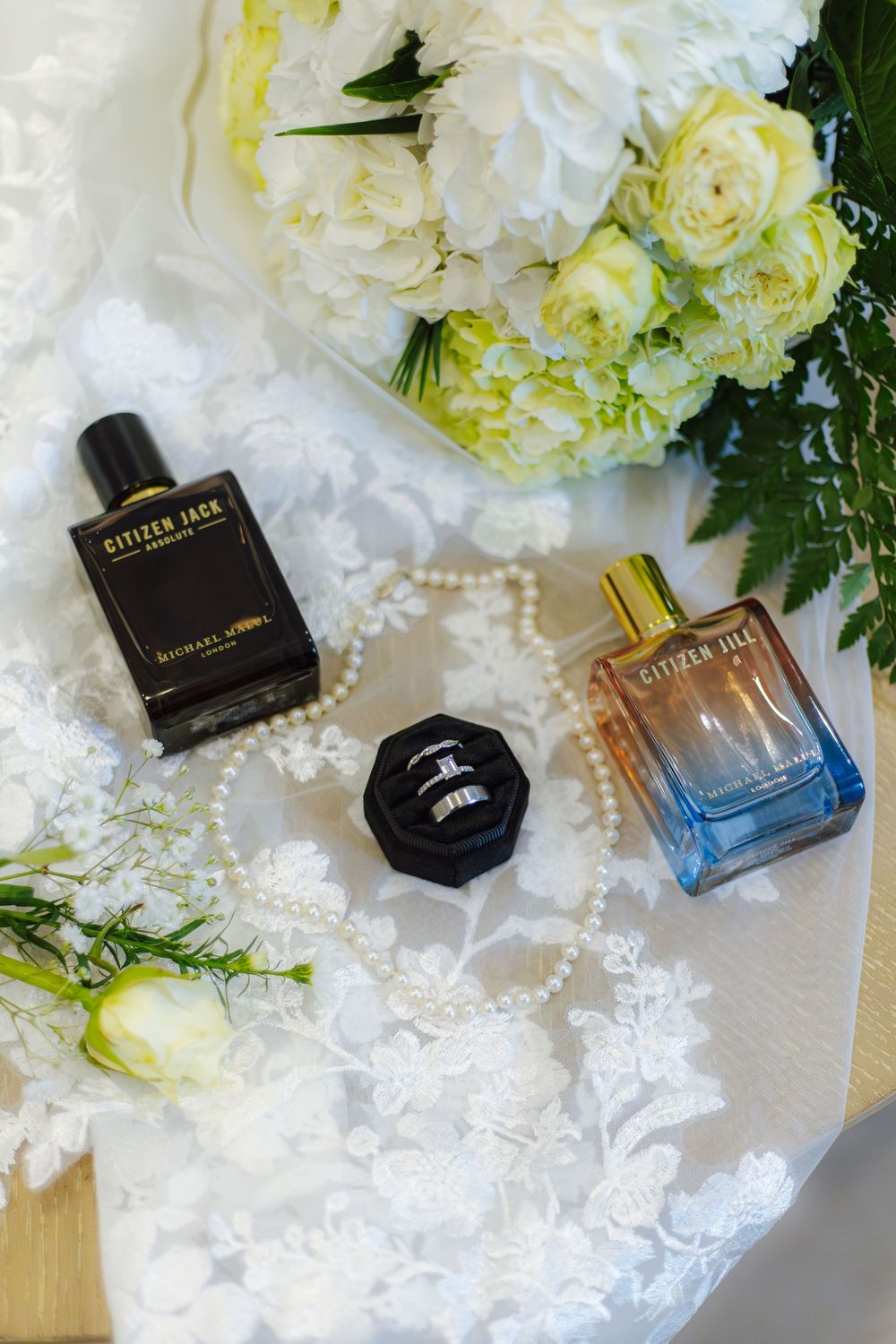 Luxury perfume bottles and white floral arrangements displayed on delicate lace fabric.