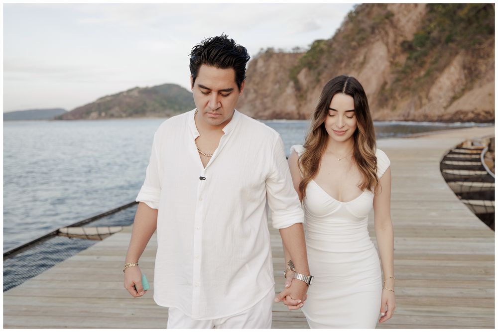 One and Only Mandarina engagement photographer with couple holding hands on a wooden pier overlooking the ocean.