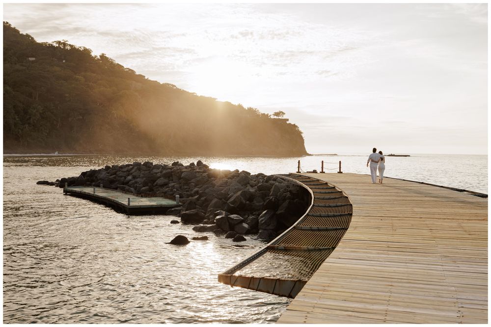 engagement photos of couple walking along a curved dock with ocean and cliffs at sunset at One and Only Mandarina.