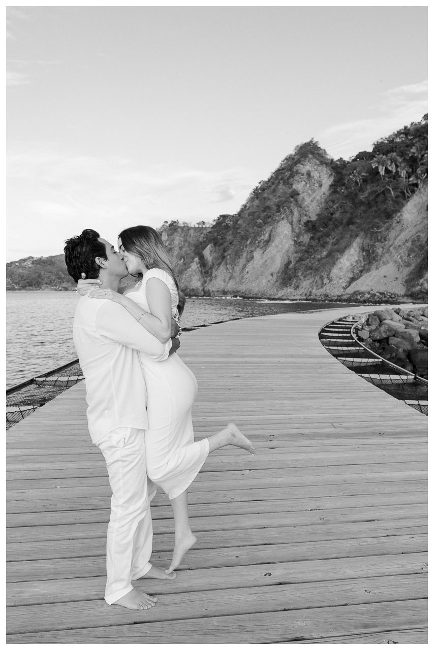Sayulita engagement photographer capturing a couple kissing on a wooden pier during romantic beach photoshoot Mexico.