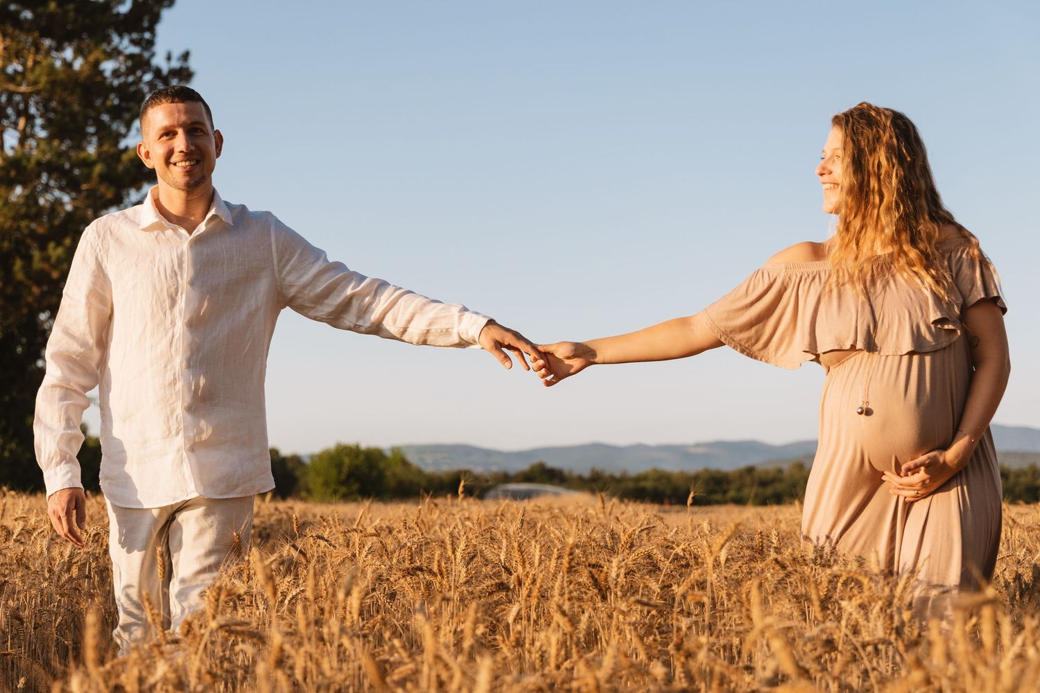 Happy couple holding hands walking through golden wheat field at sunset in Provence.