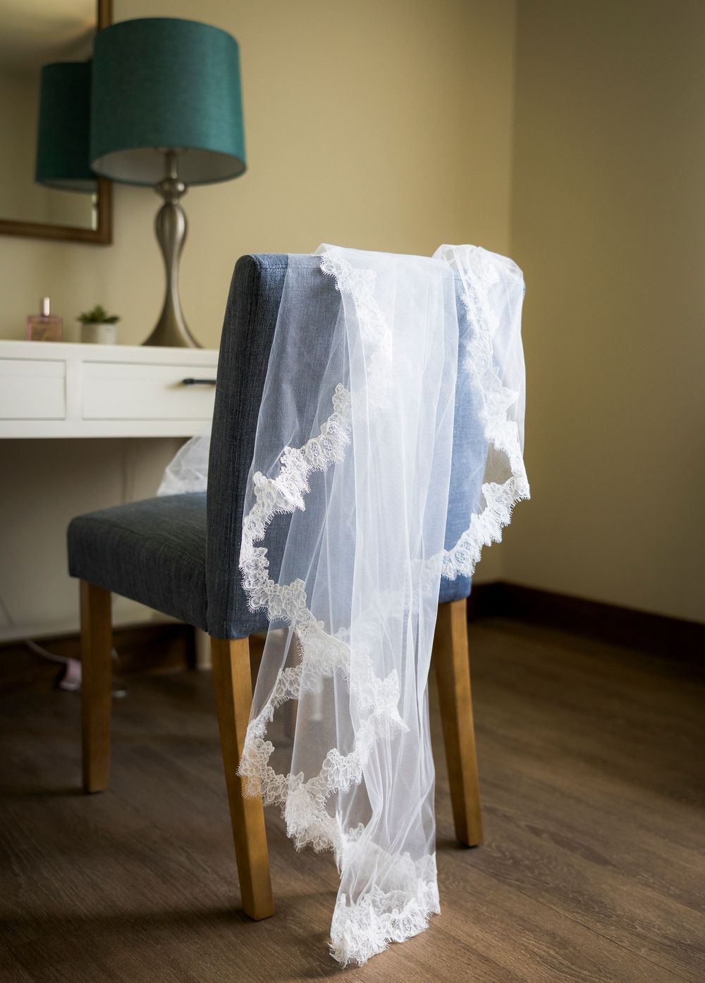 A delicate white lace wedding veil draped over a blue upholstered chair in an elegant bridal suite.