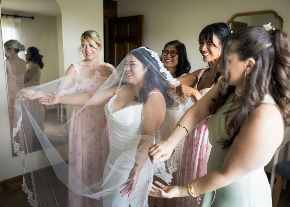 Bride laughing with bridesmaids while adjusting wedding veil during bridal preparations.