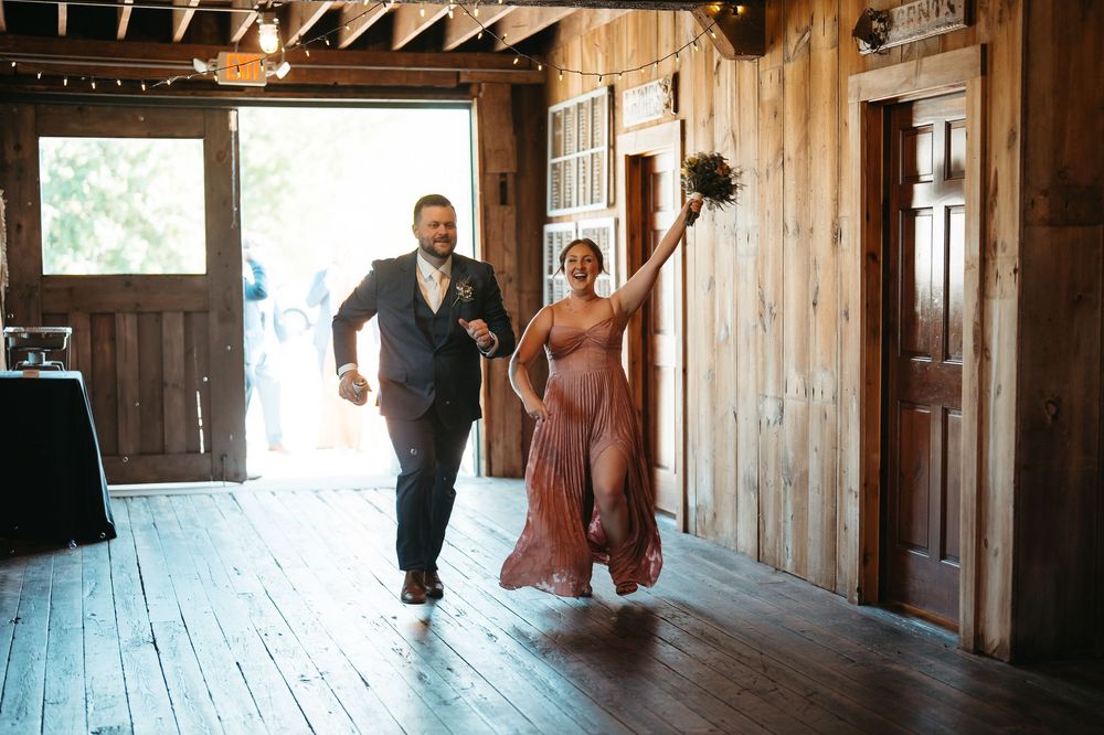 Groom and bridesmaid make a joyful grand entrance into a rustic barn wedding reception venue.