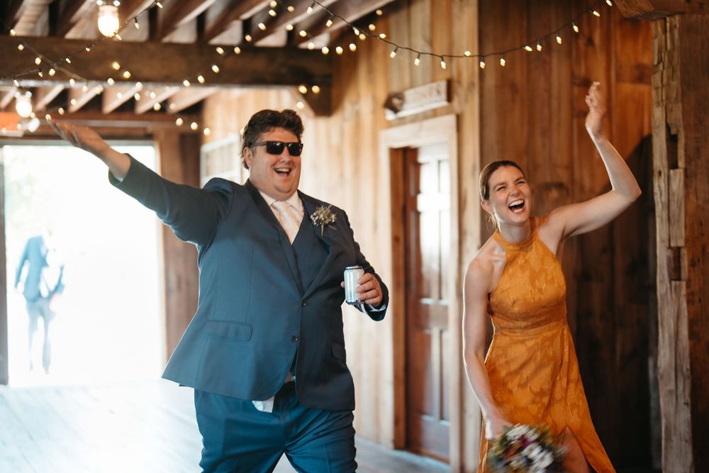 Excited wedding guests making a lively entrance into a barn reception venue with string lights.