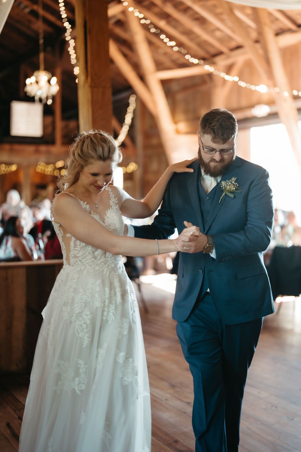Bride and groom share an emotional first dance in a rustic barn venue decorated with twinkling string lights.