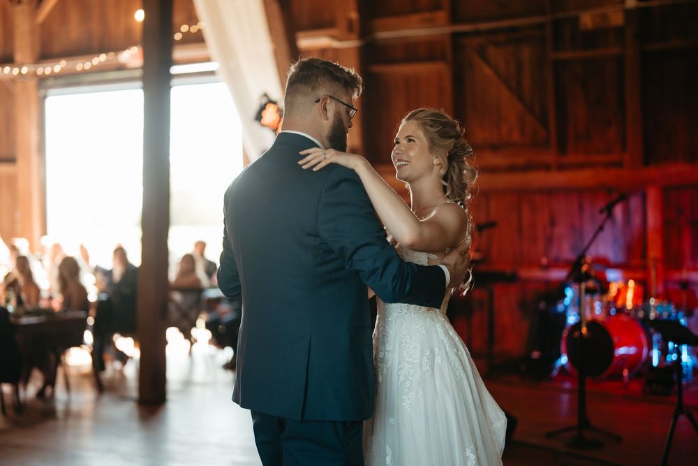 Bride and groom share their first dance in a warmly lit rustic barn wedding venue.