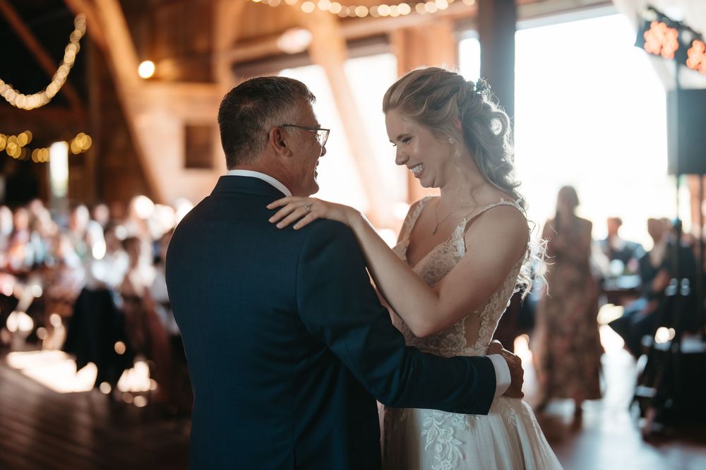 Bride shares an emotional first dance with a guest in a warmly lit rustic barn wedding reception venue.