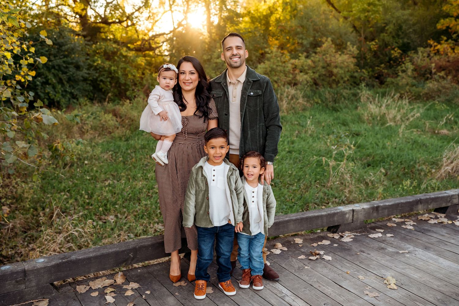 Family of five smiling together on a blanket in a sunflower field during golden hour.