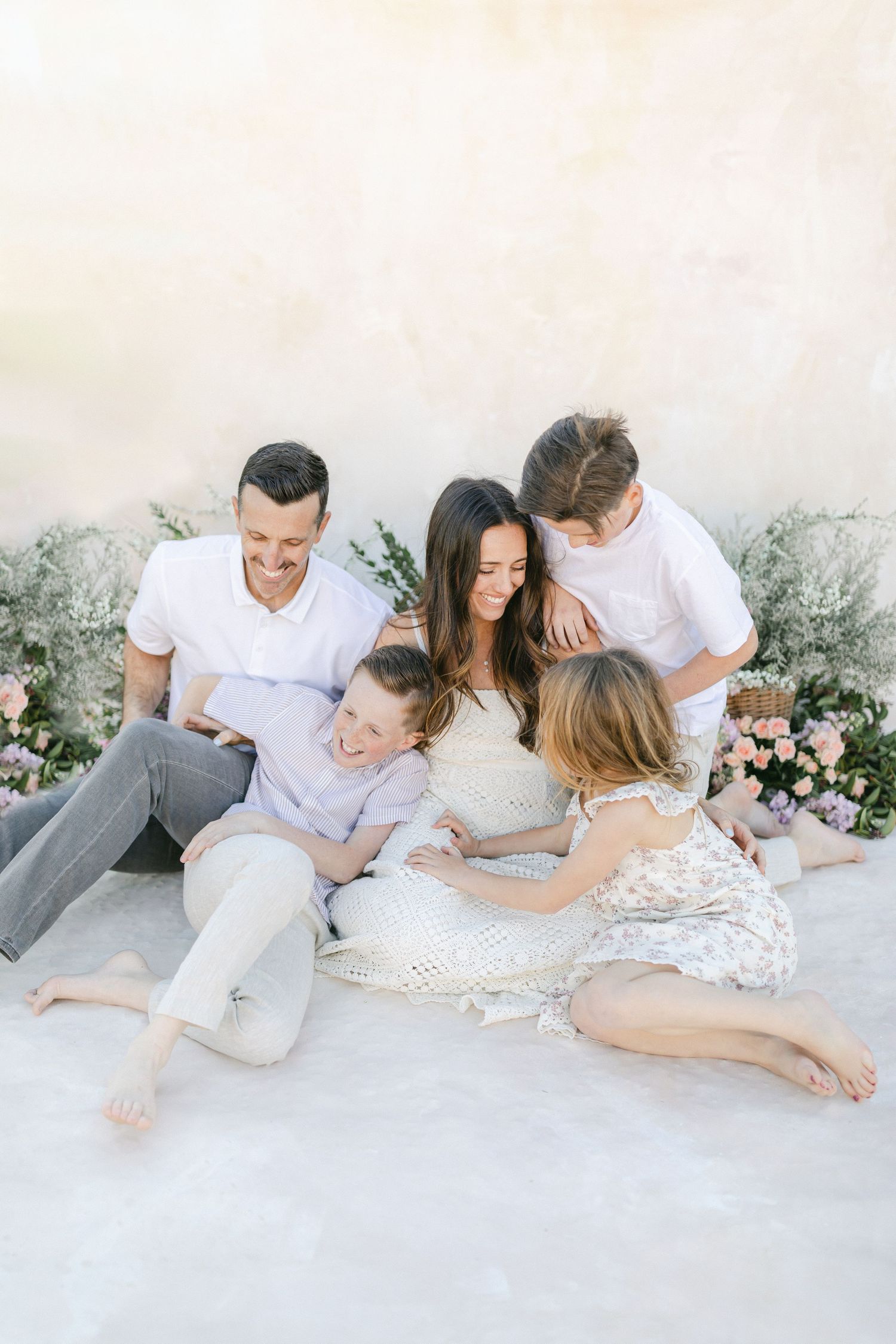 Family of five posing on farmhouse porch with white siding and metal roof on sunny day.