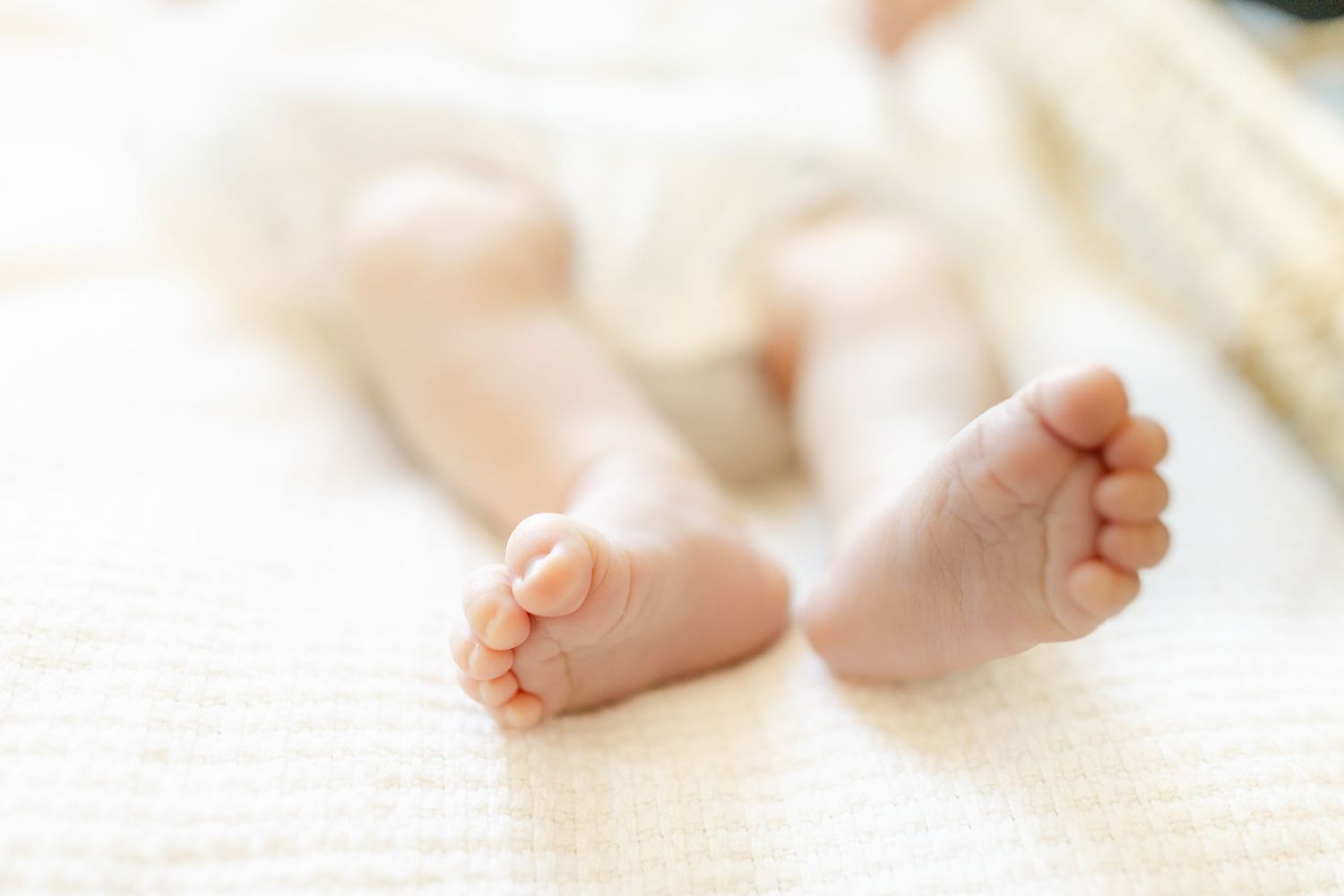 Newborn baby girl in white onesie and mint bow headband lying in wicker bassinet with parent's hands cradling her.