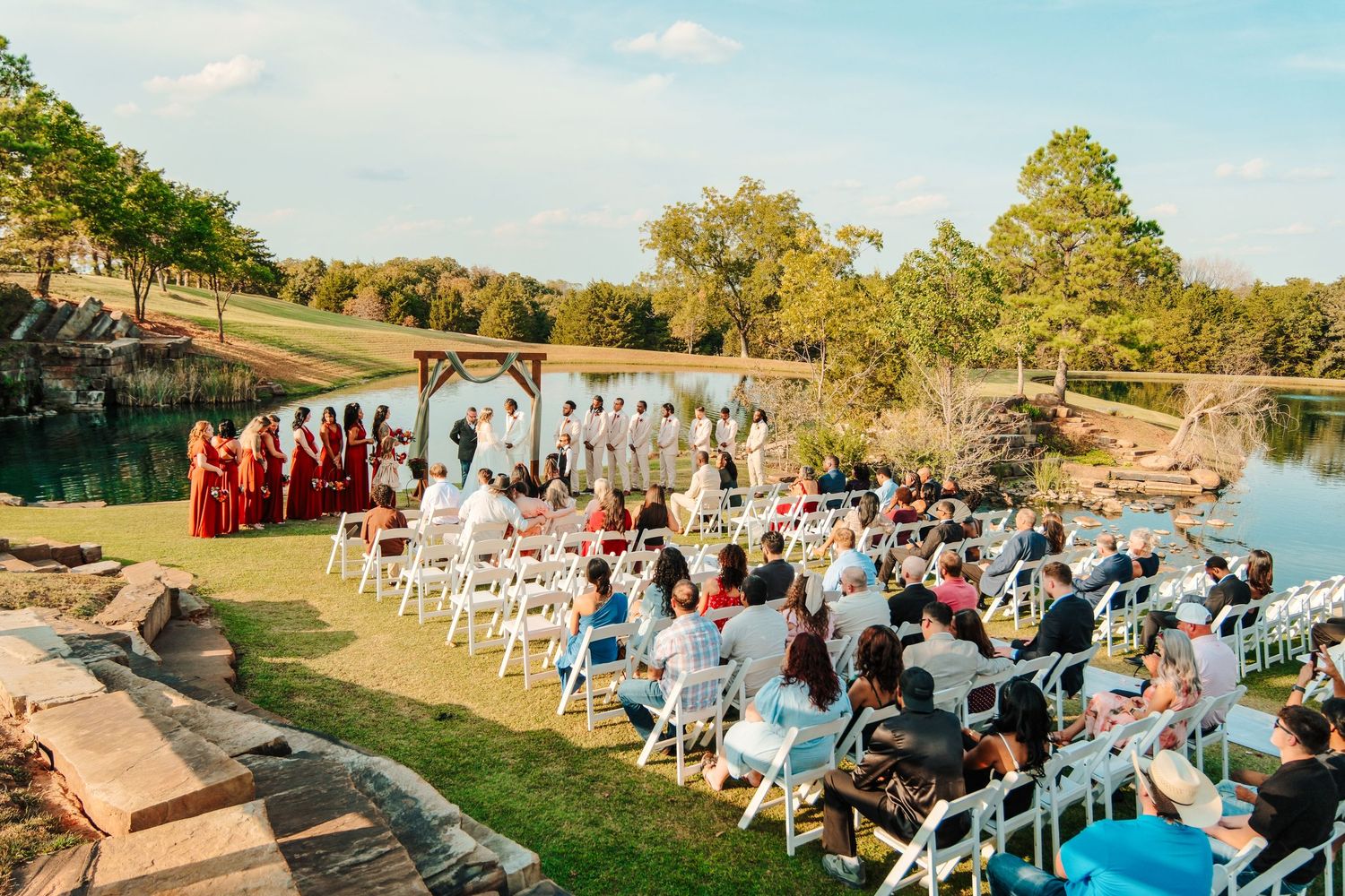 Bride and groom hold hands at altar beneath wooden cross in charming vine-covered greenhouse chapel.