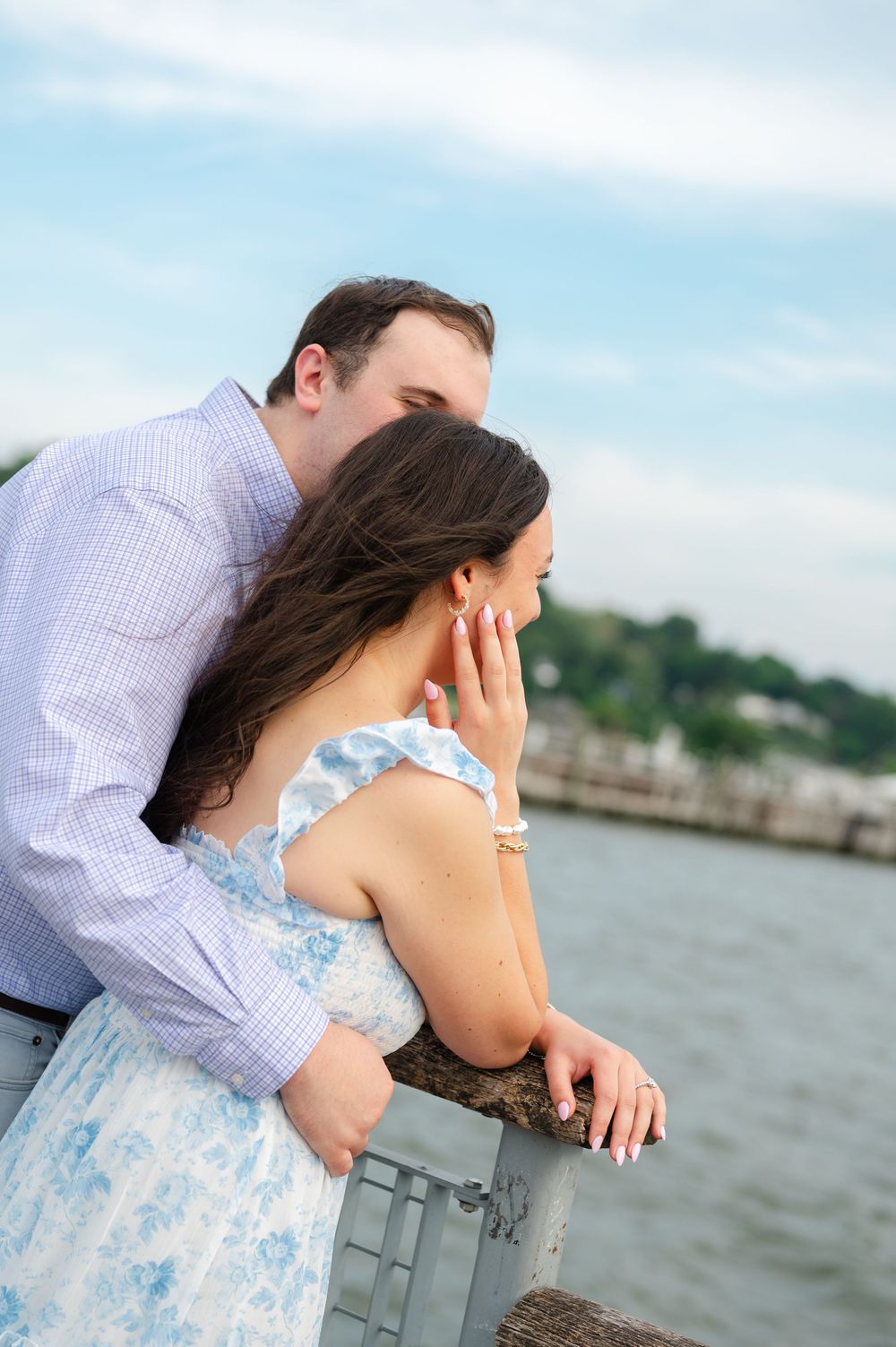 Couple leaning on a railing overlooking the water, woman covering her mouth in an emotional moment.