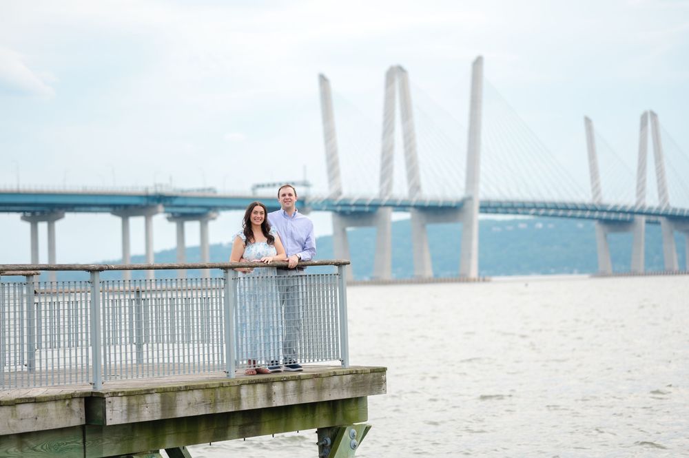 Couple standing on a wooden dock overlooking the Tappan Zee Bridge on a cloudy day.