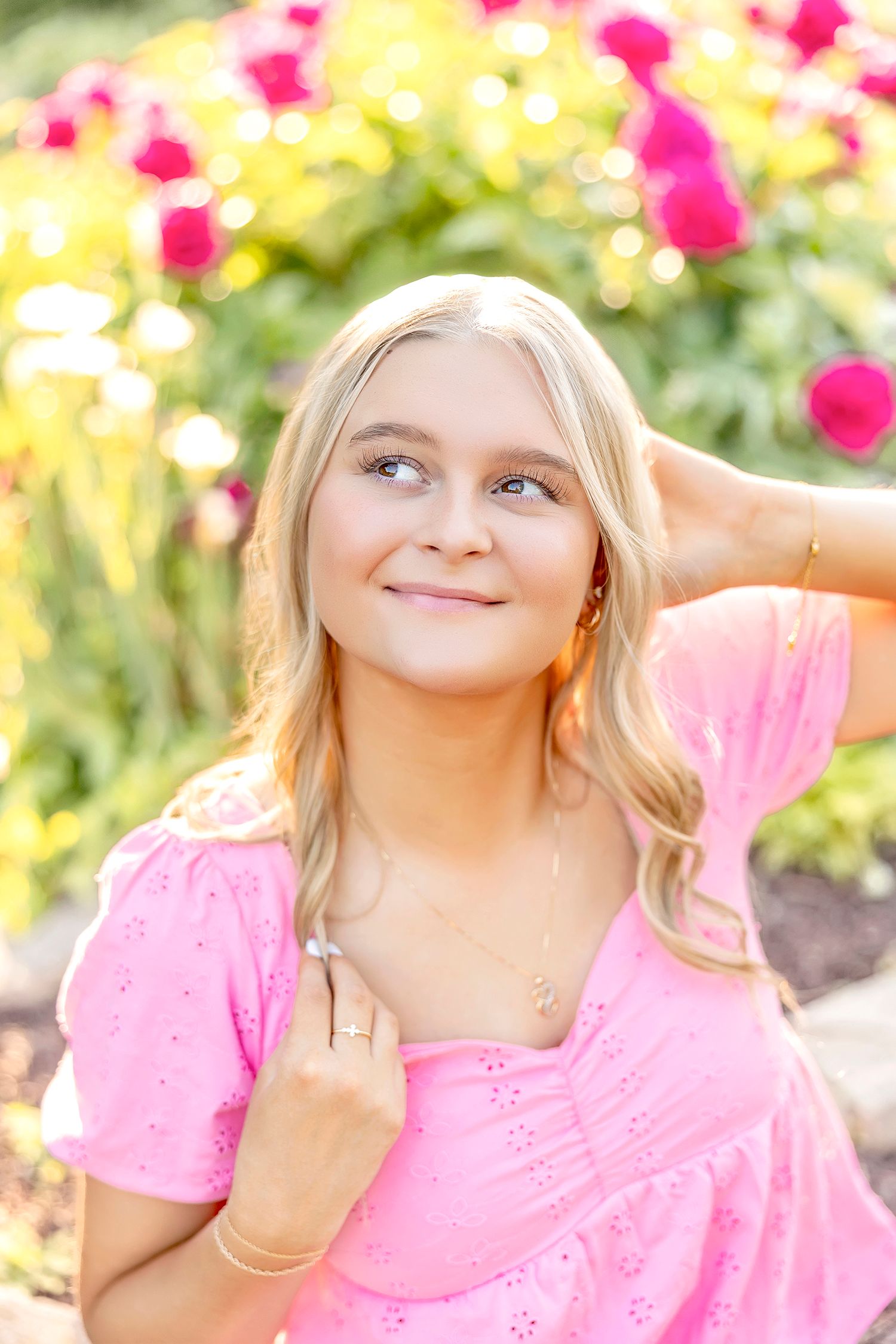 High school senior girl in a pink dress posing near colorful flowers during a summer senior photography session in Clear Lake, Iowa.