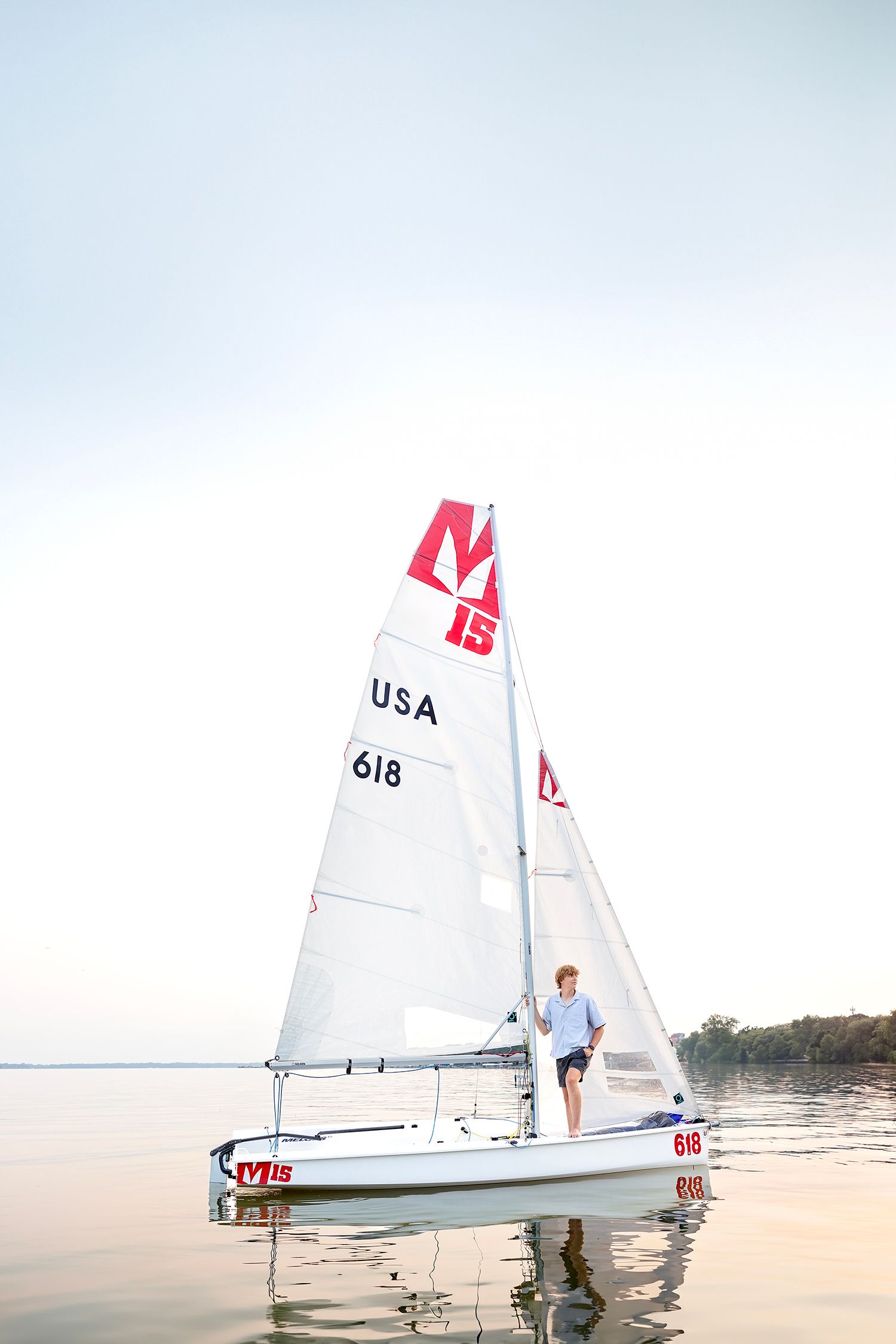 Clear Lake senior standing on a sailboat at sunset during his senior photography session on Clear Lake in Iowa.