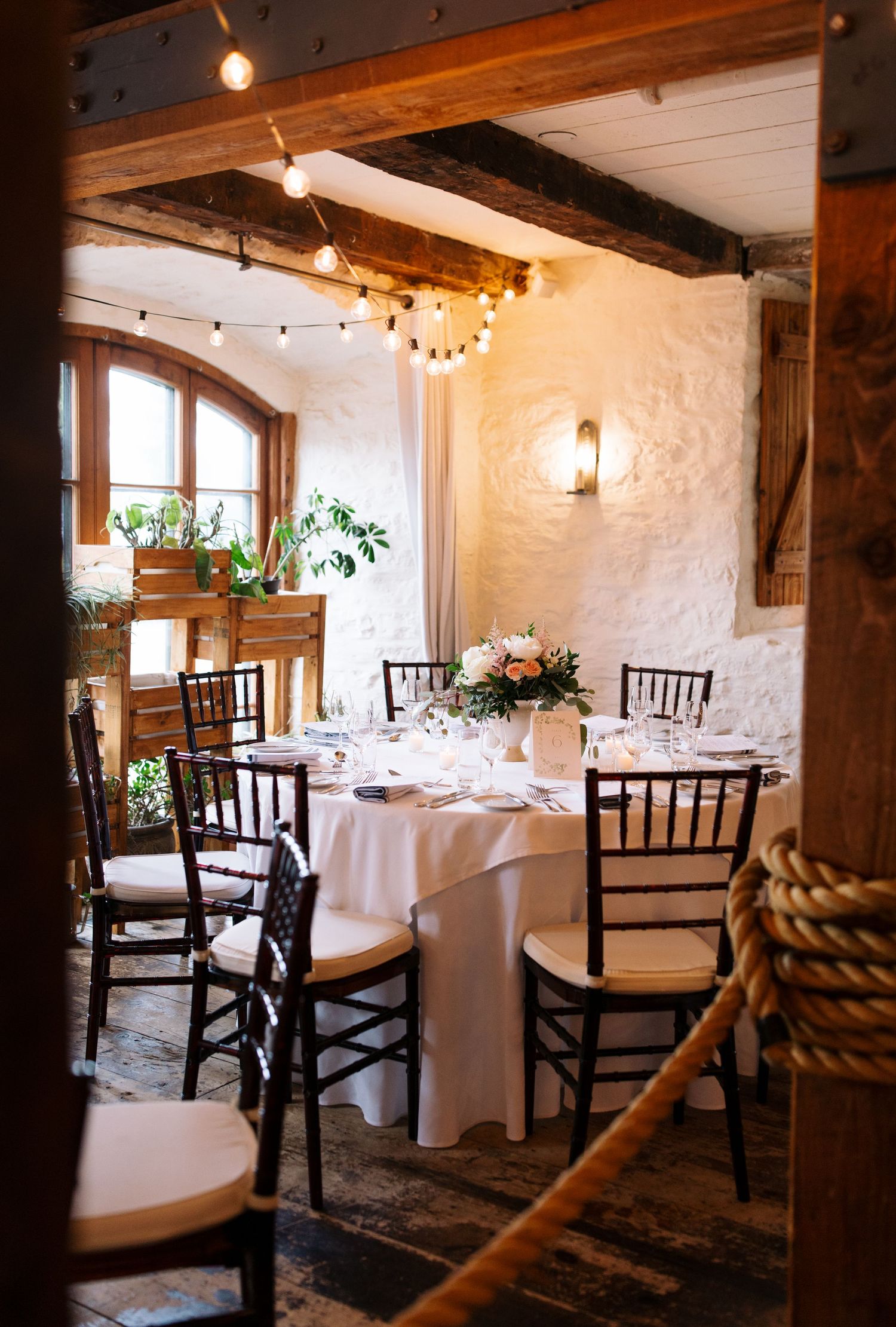 Rustic wedding reception venue with white tablecloths, dark wooden beams and string lights.