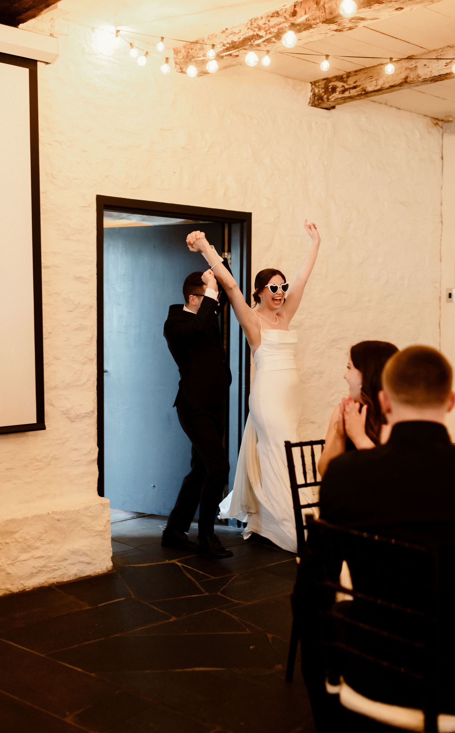 Grand entrance of wedding couple through doorway as guests cheer at rustic venue.