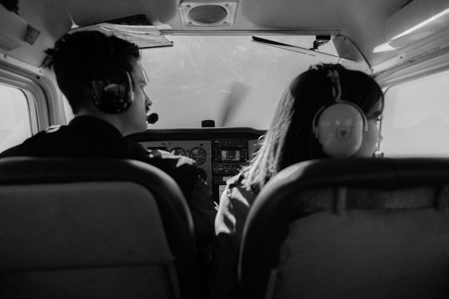 Black and white photo of a couple sitting in the cockpit of a small private airplane.