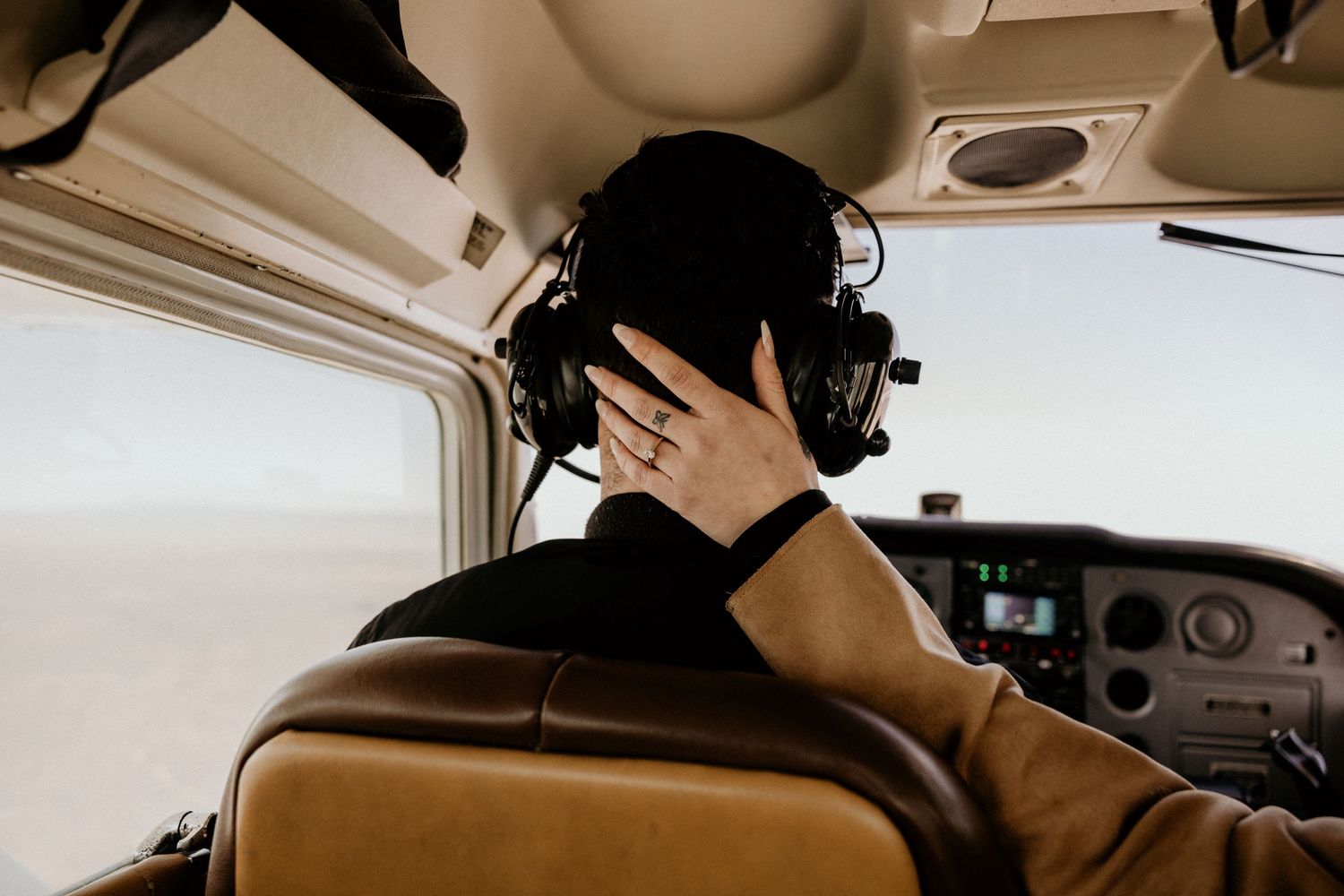 Pilot wearing headset adjusts controls in small aircraft cockpit during flight.