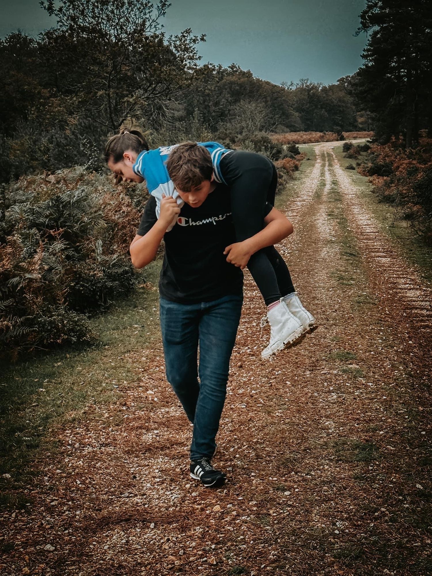 Playful couple poses for action shots on a dirt path surrounded by autumn foliage.
