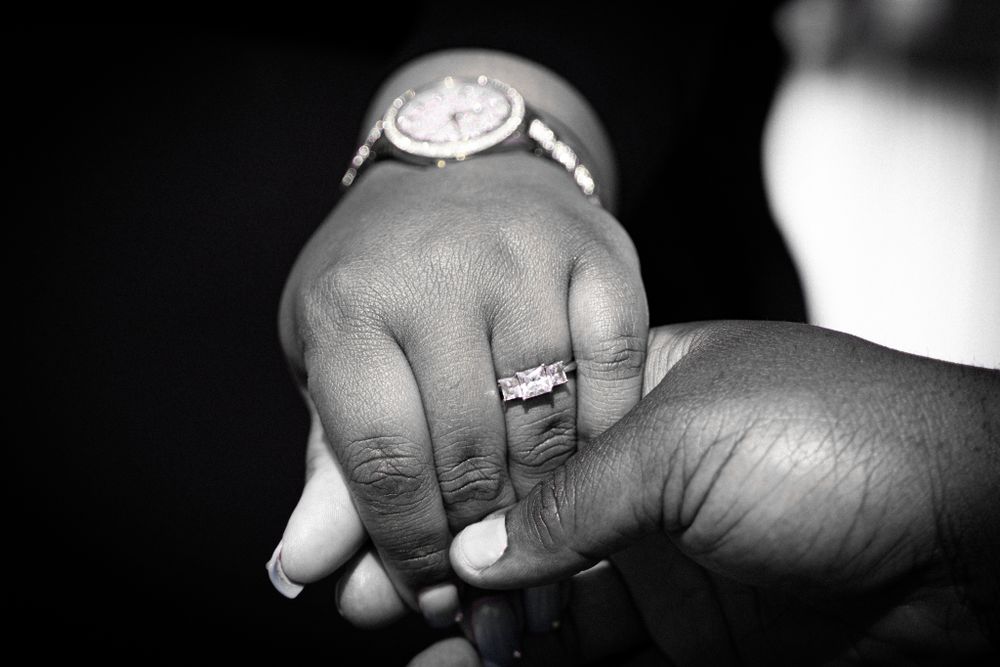 Black and white close-up of two hands holding with wedding rings and watch visible.
