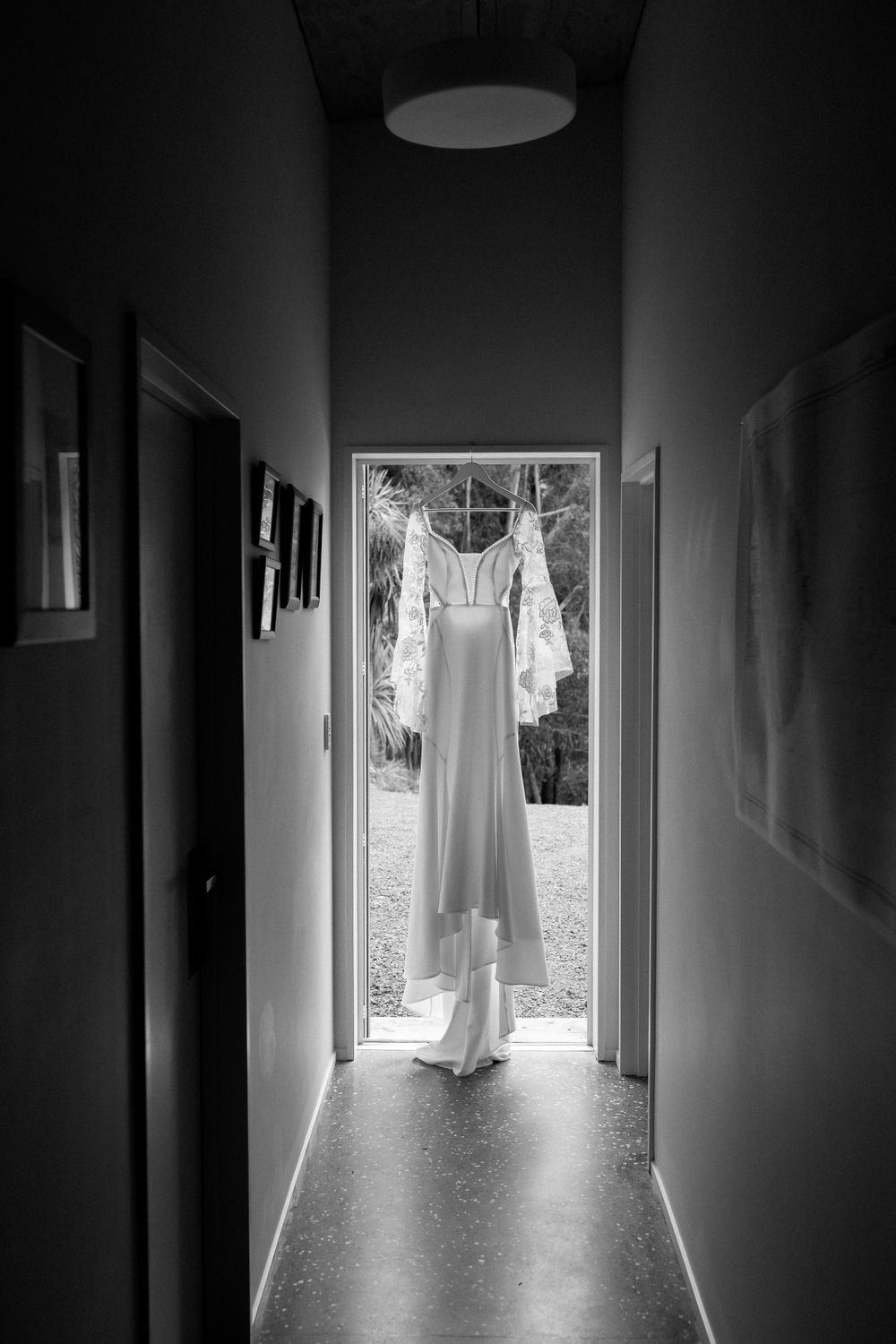 Elegant white wedding dress hanging in doorway with natural light streaming through hallway.