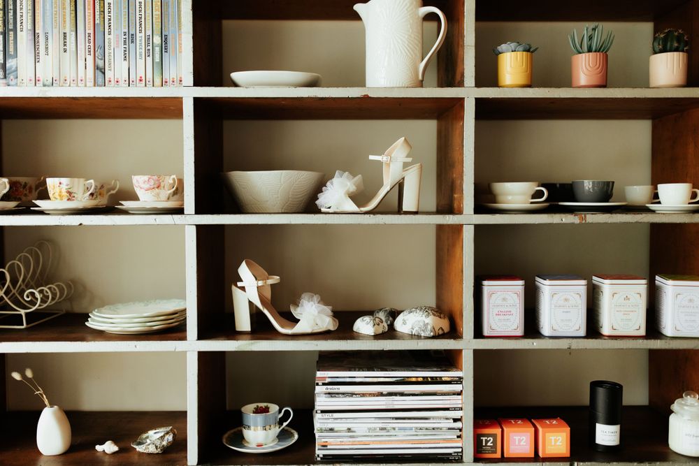 Organized shelving unit displaying white ceramics, shoes, books and decorative items.