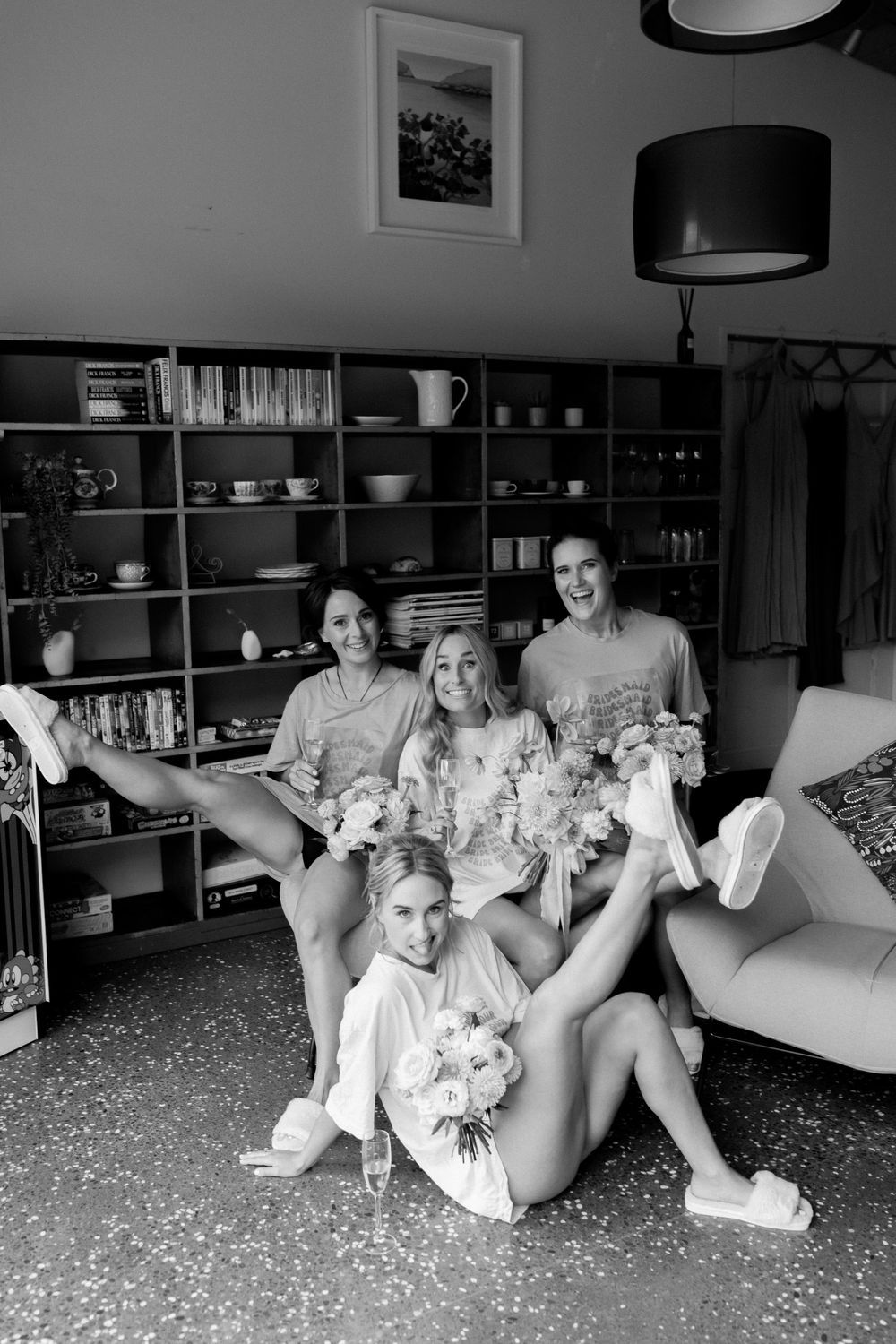 Black and white photo of group posing with bouquets in modern interior setting.